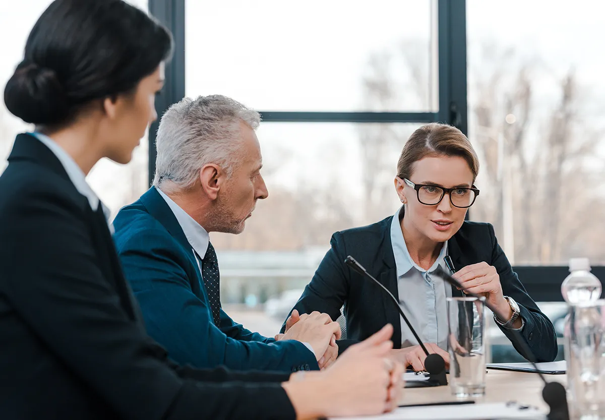 Trois personnes en tenue formelle lors d'une réunion concentrée autour d'une table de conférence.