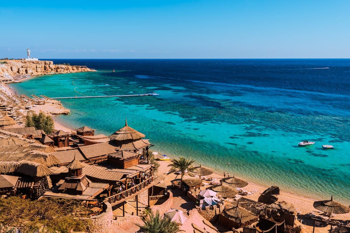 Vue aérienne d'une baie à Sharm el-Sheikh sur la mer Rouge — restaurants sur pilotis, eaux turquoises avec récifs coralliens visibles, embarcadères.
